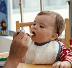 よだれかけをして離乳食を食べる金髪の外国人の赤ちゃん
